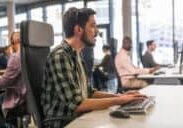 Side view of customer service representative wearing wireless headset working on desktop computer in call centre.